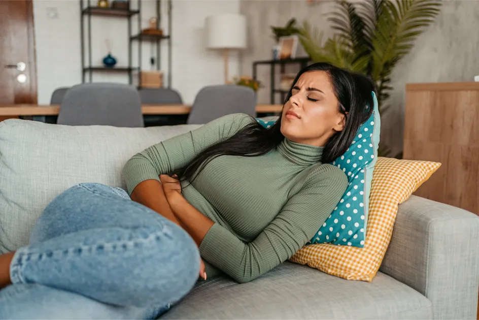 woman curled up on on couch visibly distraught with an upset stomach